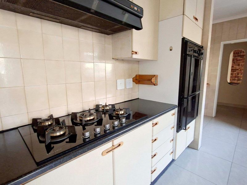 A functional kitchen featuring a gas hob, extractor fan, built-in oven, and ample cabinetry with stone countertops and tiled backsplash.