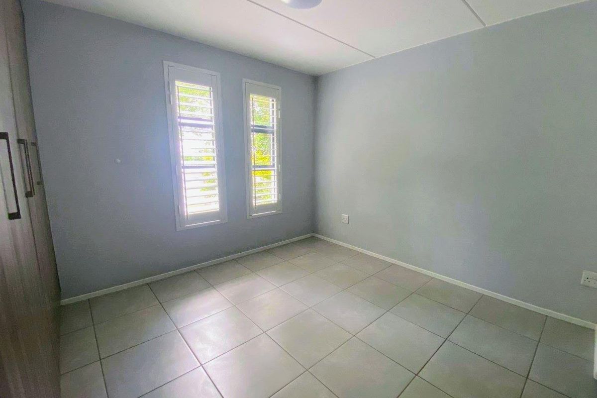 A bright, empty bedroom featuring neutral tiled flooring, built-in cupboards, and window shutters, providing a clean and versatile space.