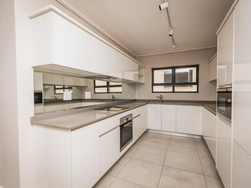 Modern kitchen featuring sleek white cabinetry, stone countertops, integrated appliances, a mirrored splashback, and neutral tiled flooring in a clean, minimalist layout.