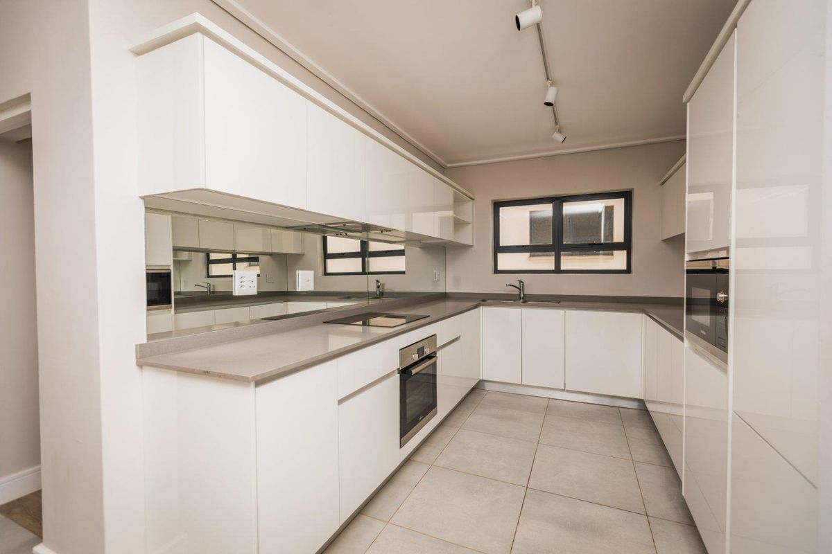 Modern kitchen featuring sleek white cabinetry, stone countertops, integrated appliances, a mirrored splashback, and neutral tiled flooring in a clean, minimalist layout.