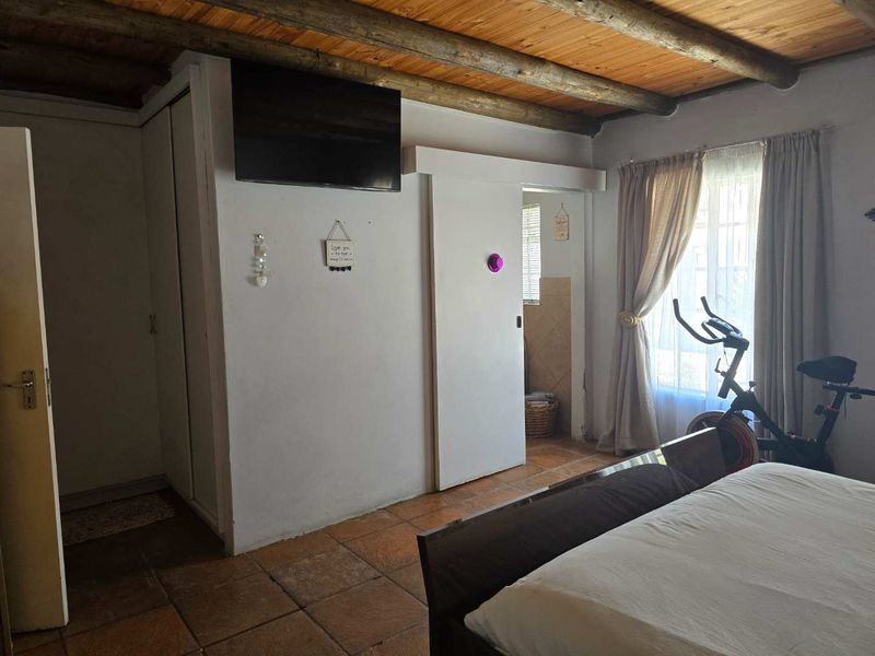 Bedroom featuring exposed timber beam ceilings and terracotta floor tiles, with an adjoining en-suite bathroom access via a sliding door.