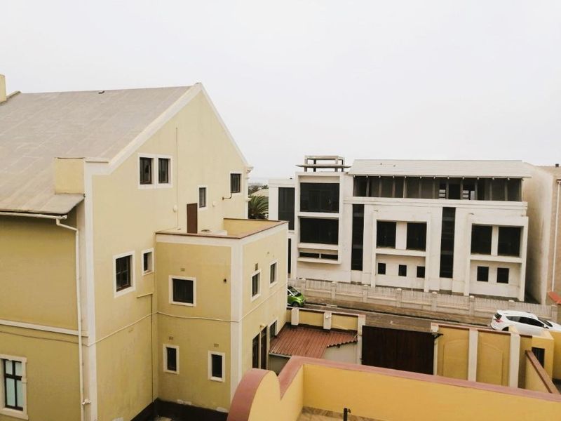 An elevated view of the rear exterior of the apartment building, showing the roof structure, facade, and surrounding neighborhood buildings.