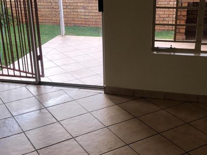 An open-plan living area featuring tiled flooring and a sliding door providing direct access to a private patio and garden area.