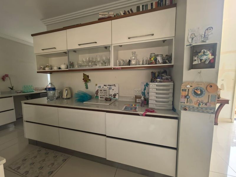 A modern kitchen featuring white handleless cabinetry, stone countertops, and glass-fronted display shelving, providing a clean and functional workspace.