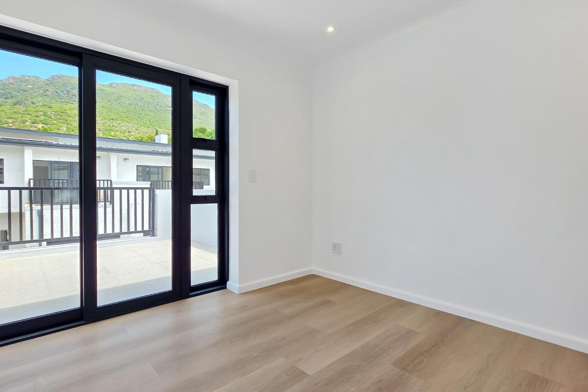 A bright, empty bedroom featuring modern light wood-look flooring, crisp white walls, and large black-framed sliding doors opening onto a private balcony.