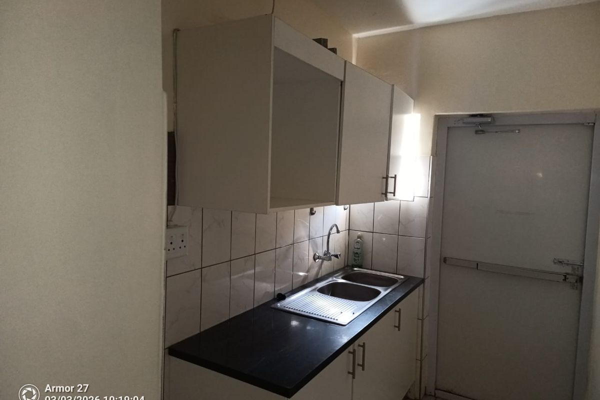 A compact kitchenette area featuring a stainless steel sink, dark countertop, and white wall-mounted cabinetry with tiled splashbacks.