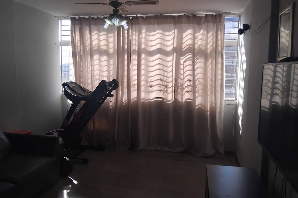 A living room area featuring large windows with curtains, a ceiling fan, and tiled flooring, providing a functional space for relaxation.