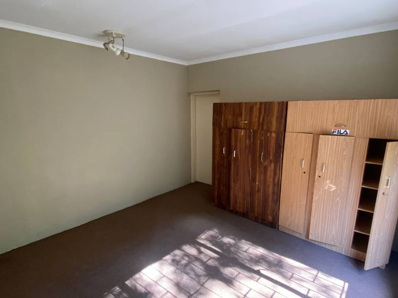 A bedroom featuring built-in cupboards, carpeted flooring, and security bars on the window. The space offers a functional layout ready for modernization.