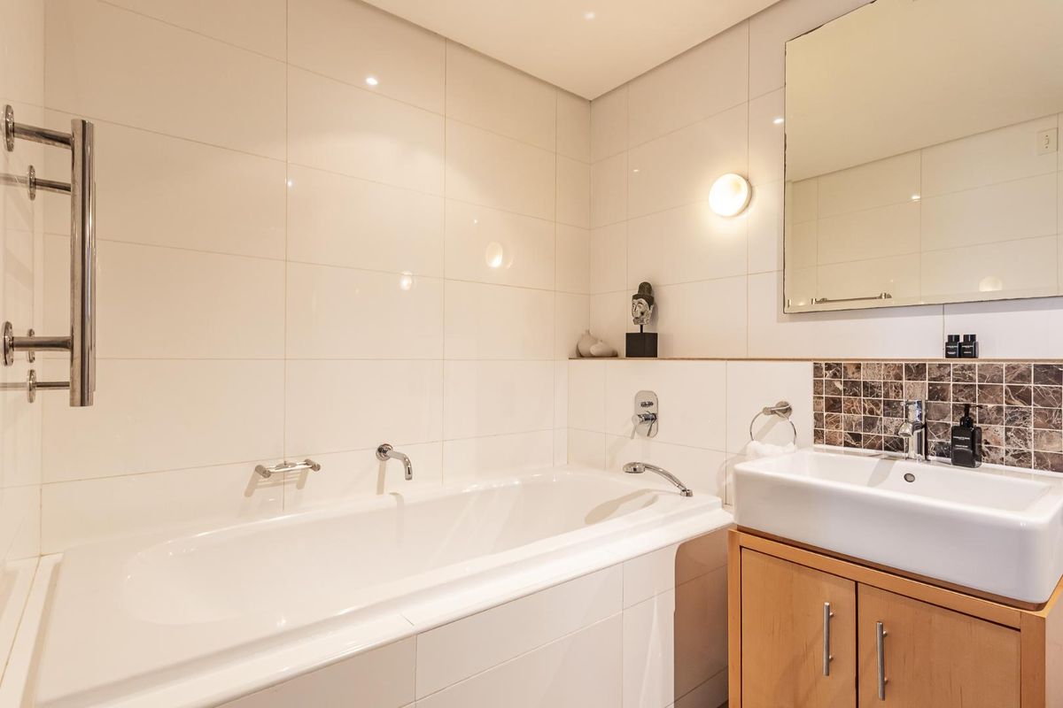 Modern bathroom featuring a built-in bathtub, wall-mounted fixtures, a vanity cabinet with a ceramic basin, and a heated towel rail.