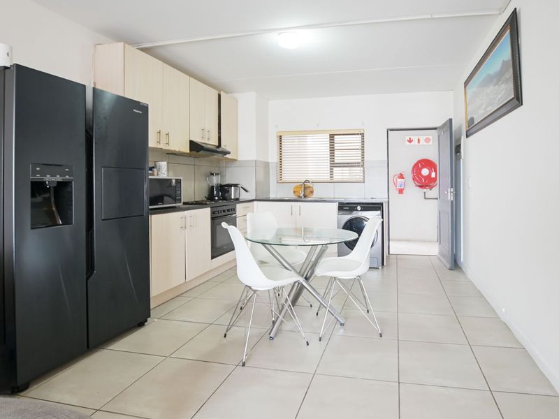 Functional kitchen featuring light wood cabinetry, tiled flooring, integrated appliances, and direct access to a utility area with fire safety equipment.