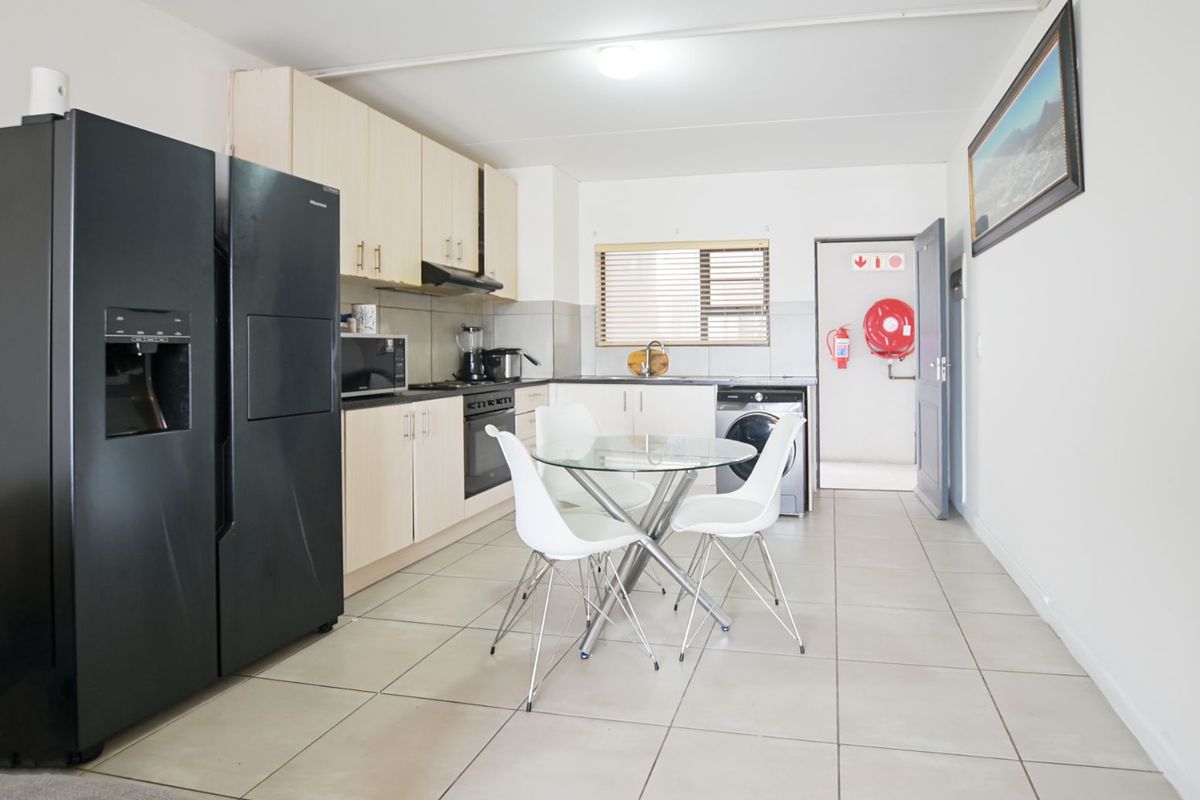 Functional kitchen featuring light wood cabinetry, tiled flooring, integrated appliances, and direct access to a utility area with fire safety equipment.