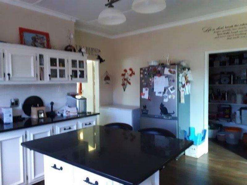 A functional kitchen featuring white cabinetry, black granite countertops, a central island, and an adjacent walk-in pantry area.