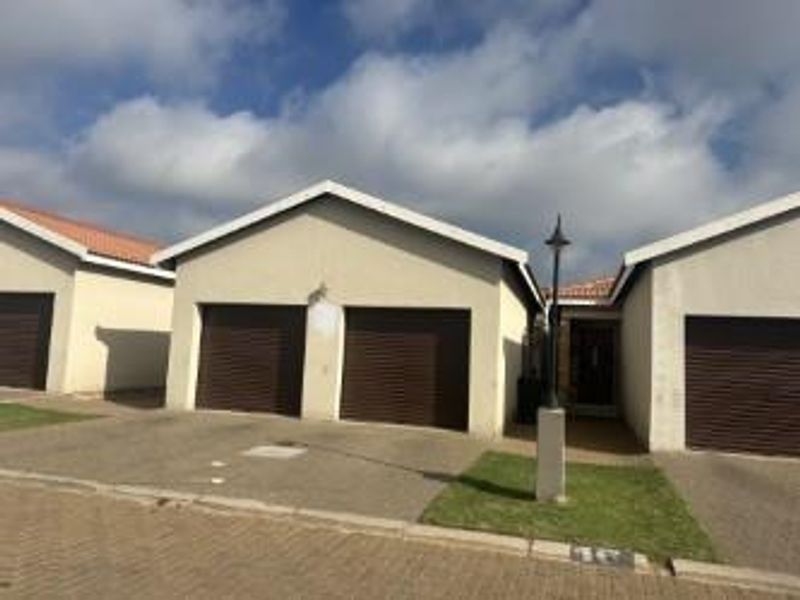 Exterior view of a townhouse featuring a double garage with roller doors, paved driveway, and a small patch of lawn.