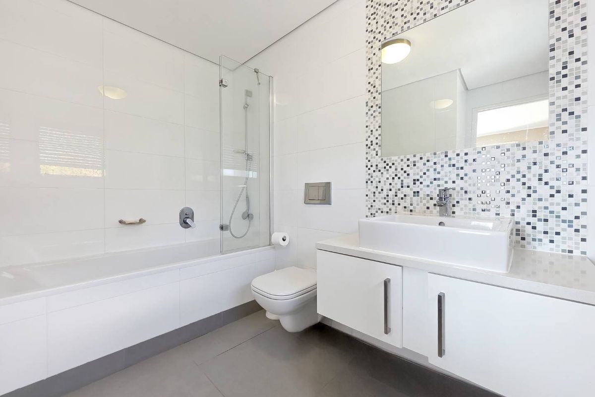 Modern bathroom featuring a floating vanity, wall-mounted toilet, built-in bathtub with glass screen, and a stylish mosaic tile feature wall.
