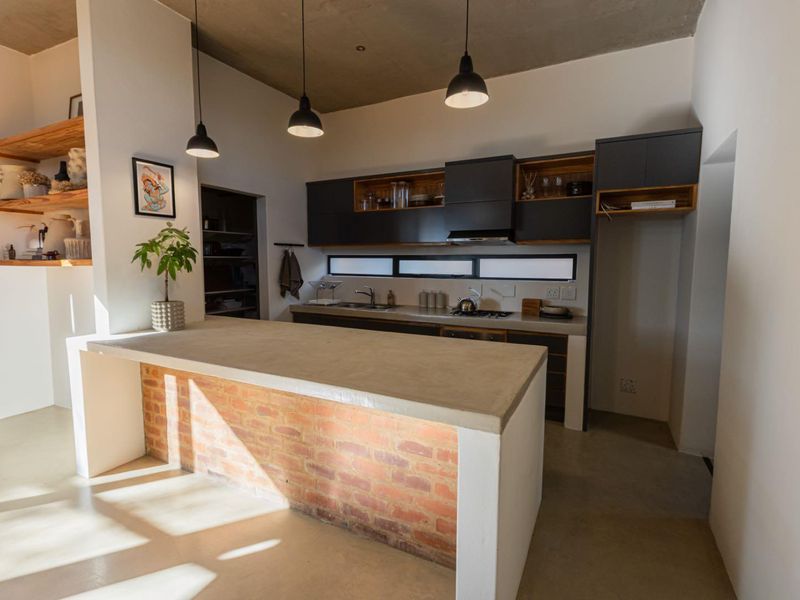 Modern kitchen featuring a concrete island with exposed brick base, sleek dark cabinetry, integrated appliances, and stylish pendant lighting under an exposed concrete ceiling.