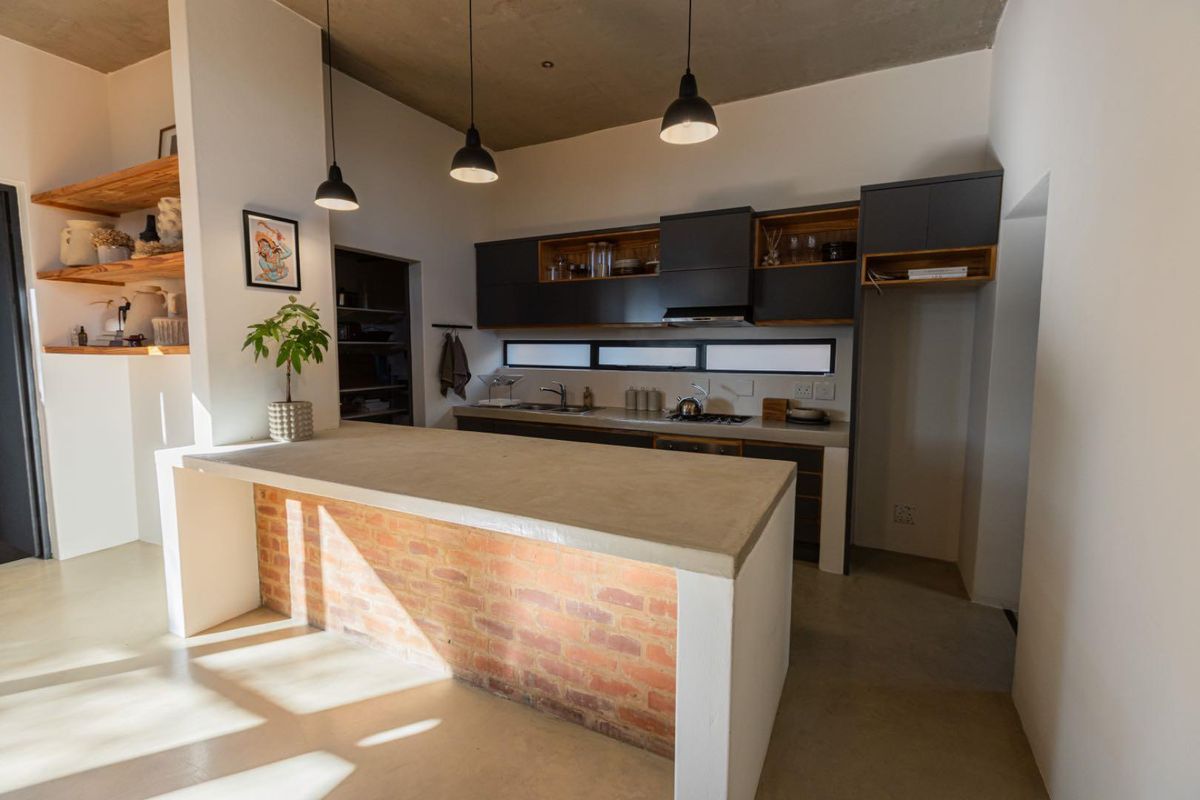 Modern kitchen featuring a concrete island with exposed brick base, sleek dark cabinetry, integrated appliances, and stylish pendant lighting under an exposed concrete ceiling.