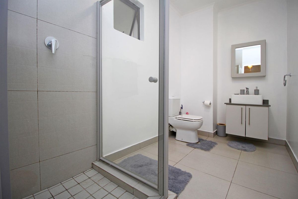 A clean, modern bathroom featuring a glass-enclosed shower, a wall-mounted vanity with a basin, and a standard toilet.