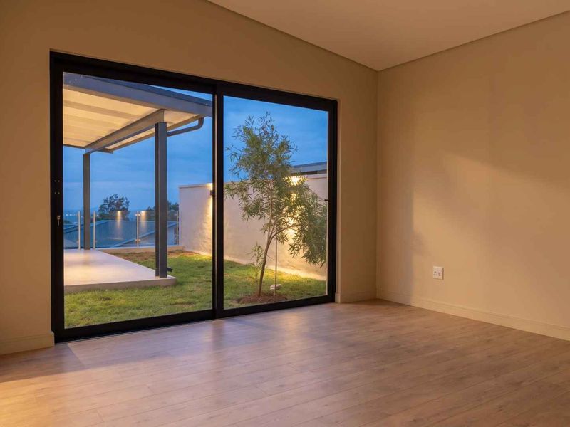 A bright, empty living room featuring modern laminate flooring and large sliding glass doors that open onto a private patio and garden area.