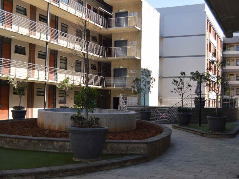 A view of the apartment complex courtyard featuring paved walkways, a central raised garden bed with a fountain, and multi-story residential building facades.