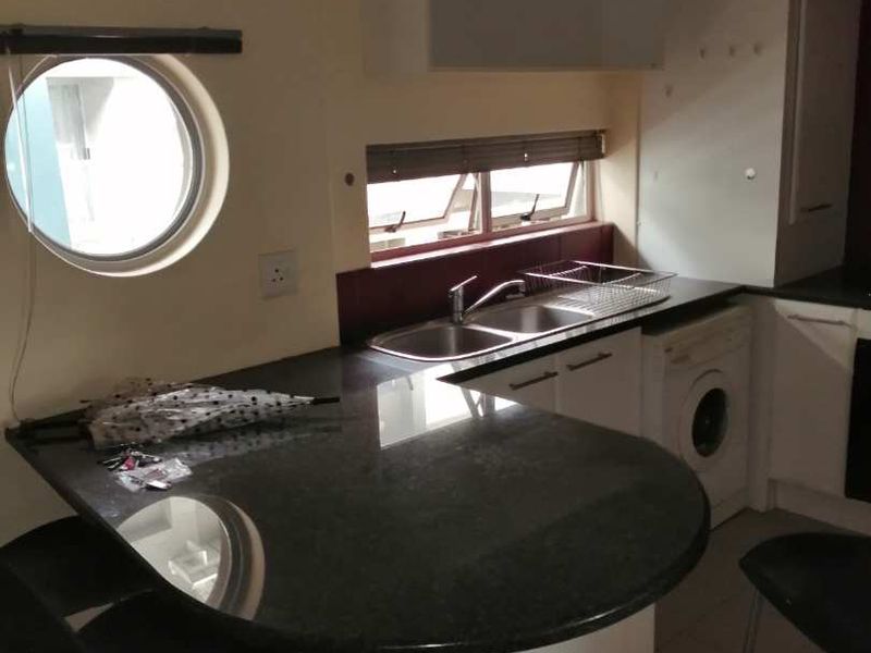 Compact kitchen featuring a granite breakfast bar, double sink, built-in cabinetry, and an integrated washing machine with a unique porthole window.