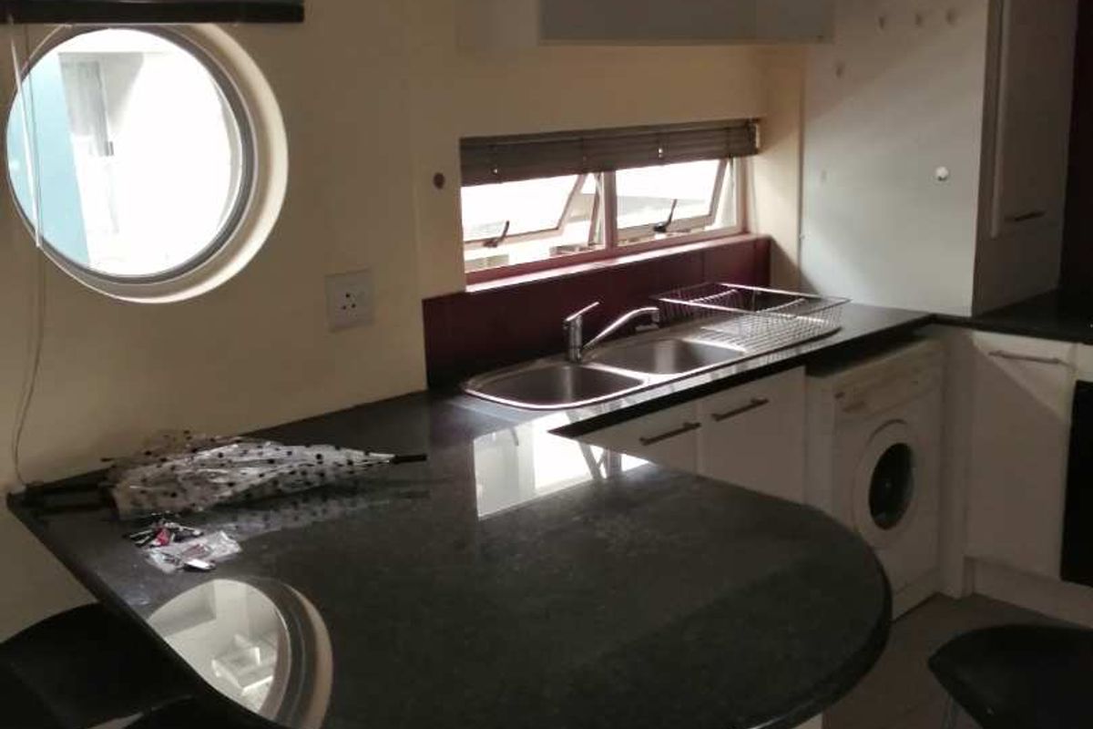 Compact kitchen featuring a granite breakfast bar, double sink, built-in cabinetry, and an integrated washing machine with a unique porthole window.