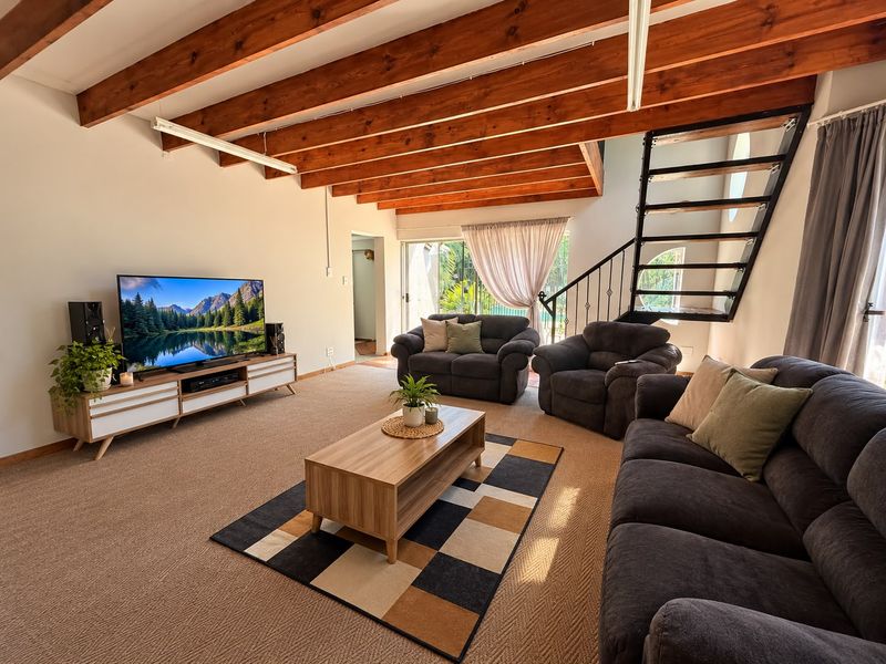 Spacious living room featuring exposed timber ceiling beams, a modern metal staircase, and large sliding glass doors leading to the outdoor area.
