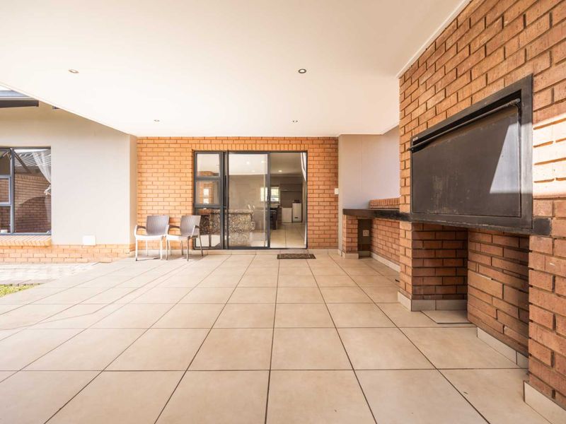 Spacious covered patio featuring a built-in braai, tiled flooring, and direct access to the interior through sliding glass doors.