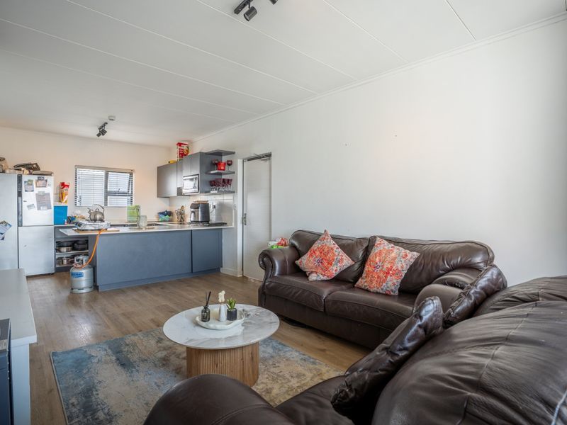 An open-plan living area featuring a modern kitchen with dark cabinetry and a central island, seamlessly flowing into a comfortable lounge space.
