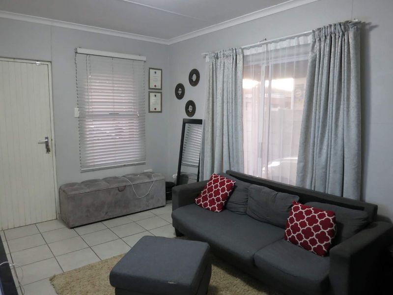A living room featuring tiled flooring, a sliding glass door with curtains, and venetian blinds, providing a functional and neutral living space.