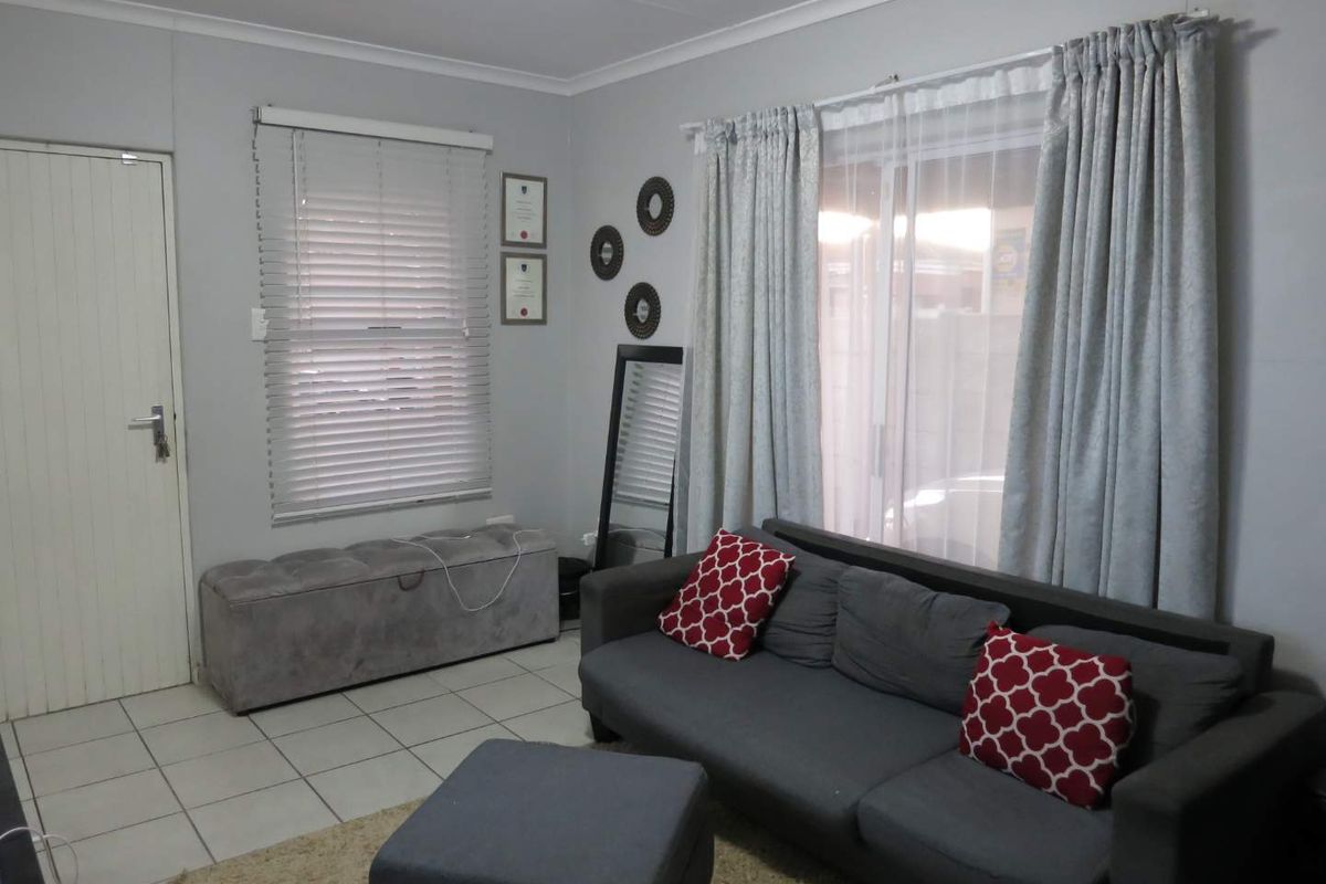 A living room featuring tiled flooring, a sliding glass door with curtains, and venetian blinds, providing a functional and neutral living space.