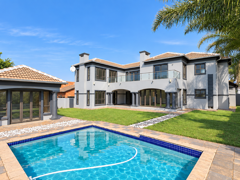 Spacious rear exterior featuring a swimming pool, landscaped garden, detached pool house, and a large two-story home with a balcony and patio.