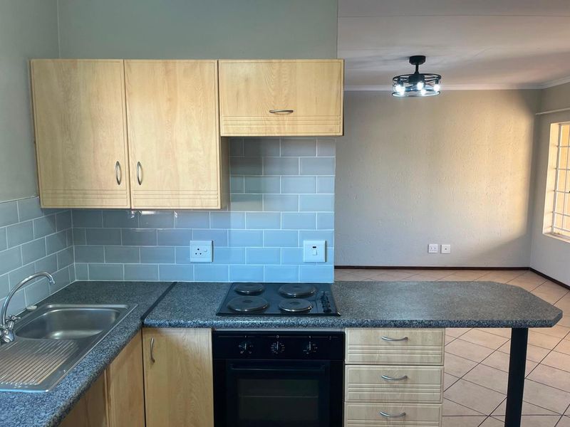 Open-plan kitchen featuring light wood cabinetry, granite-look countertops, subway tile backsplash, and integrated electric cooking appliances, flowing into an adjacent living area.