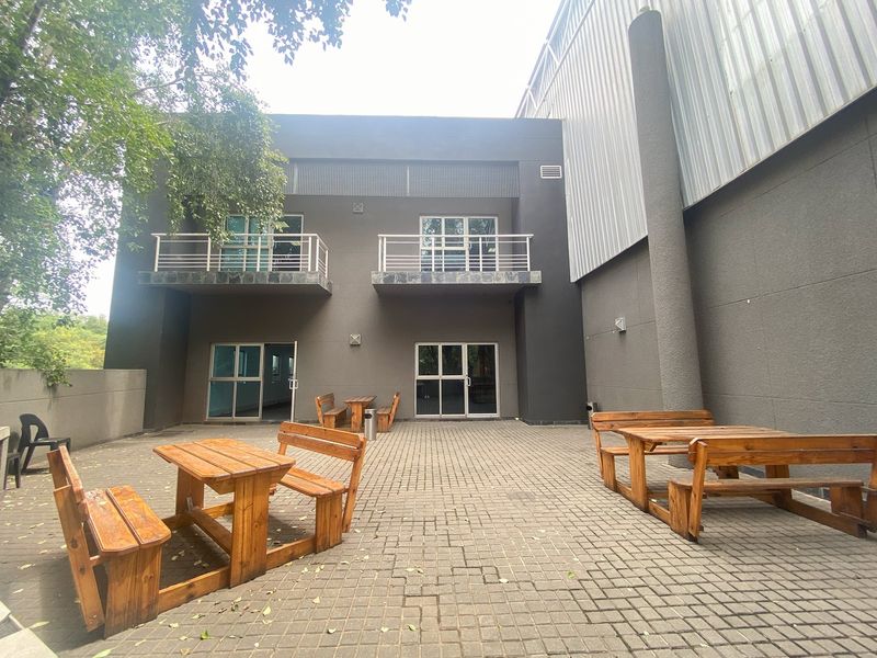 A paved rear courtyard area featuring industrial-style metal cladding, two upper-level balconies, and multiple access points via sliding glass doors.