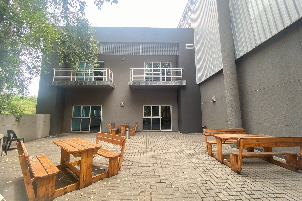 A paved rear courtyard area featuring industrial-style metal cladding, two upper-level balconies, and multiple access points via sliding glass doors.