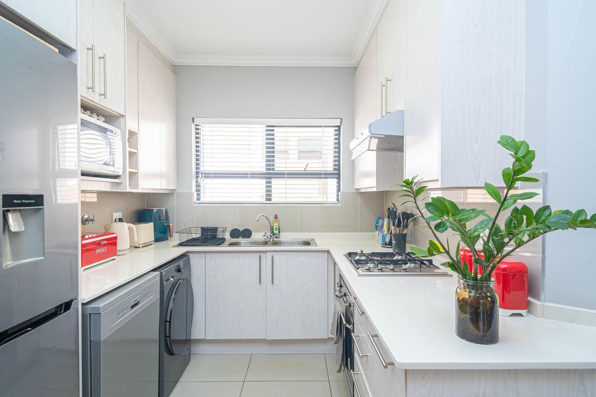 A well-maintained galley-style kitchen featuring light wood-grain cabinetry, stone countertops, a gas hob, and an integrated extractor fan.