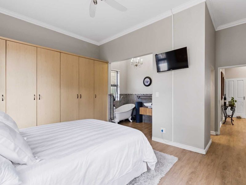 Spacious bedroom featuring extensive built-in cupboards, laminate flooring, and an open-plan en-suite bathroom with a classic freestanding bathtub and vanity.