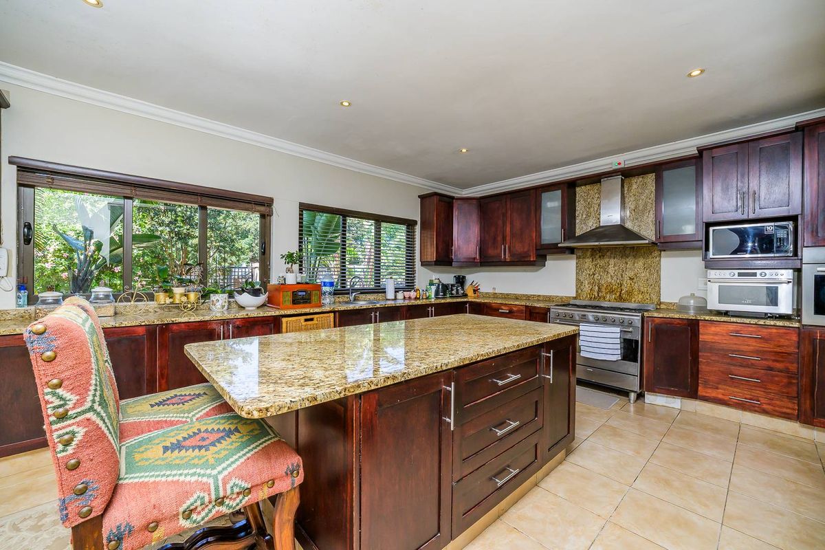 Spacious kitchen featuring dark wood cabinetry, granite countertops, a central island, and stainless steel appliances, including a built-in oven and extractor fan.