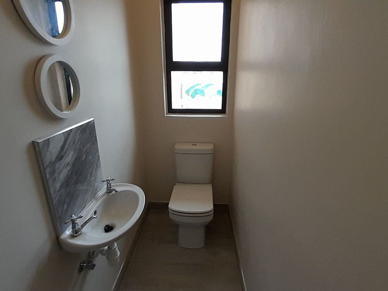 A compact guest bathroom featuring a modern toilet, a wall-mounted washbasin with a marble-look splashback, and a window for natural light.