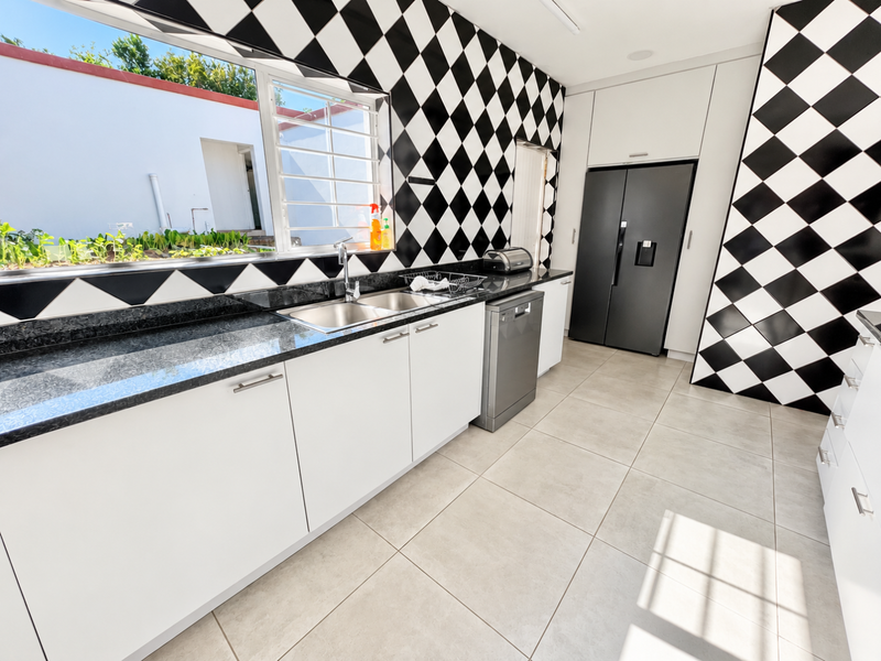 Modern kitchen featuring striking black and white checkered wall tiles, granite countertops, stainless steel sink, and integrated dishwasher with ample storage cabinetry.