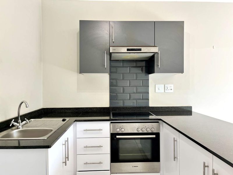 Modern kitchen featuring granite countertops, subway tile backsplash, built-in oven, electric hob, extractor fan, and ample white and grey cabinetry.