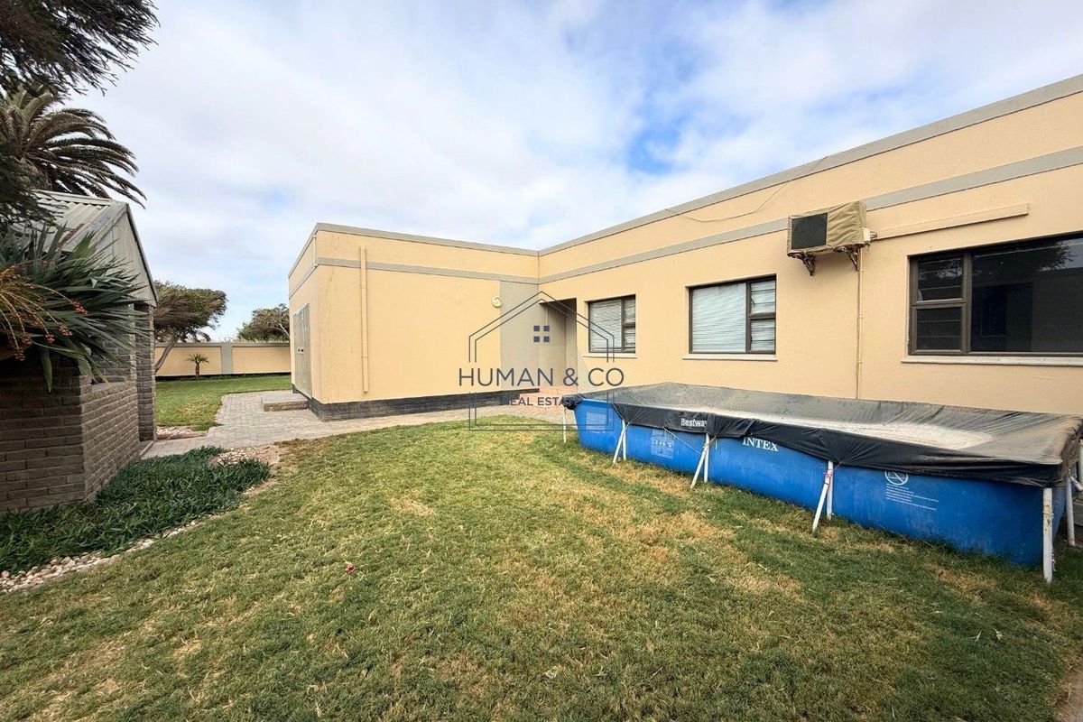 Rear view of the property featuring a lawn area, paved walkway, and exterior wall with mounted air conditioning unit.