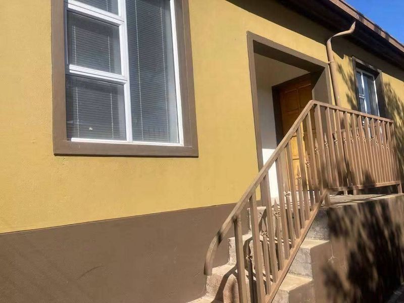 Exterior view of the property entrance featuring concrete steps with a metal railing and aluminium window frames.