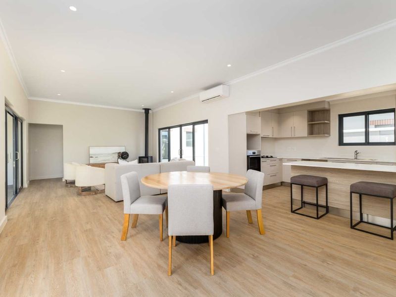 Spacious open-plan living and dining area featuring modern kitchen cabinetry, a central island, wood-burning fireplace, and seamless access to outdoor spaces.