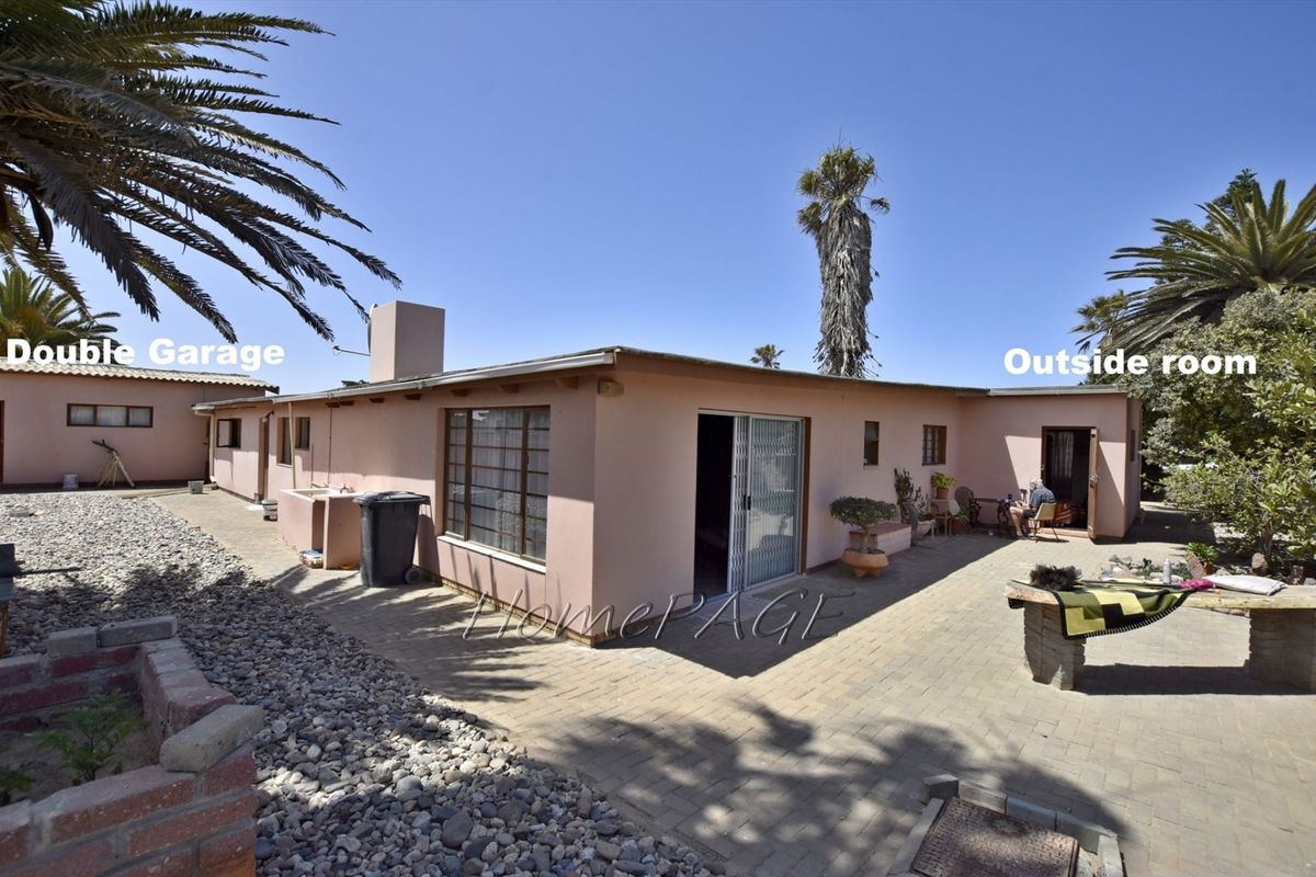 Rear exterior view of the property featuring a paved courtyard, sliding glass doors, and access to a double garage and separate outside room.