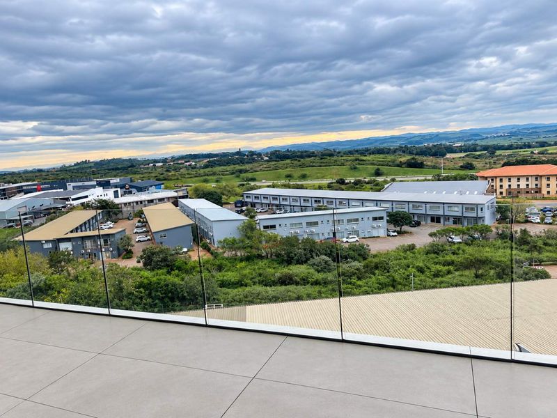 Elevated aerial view overlooking a commercial business park complex with surrounding green landscape and distant hills.