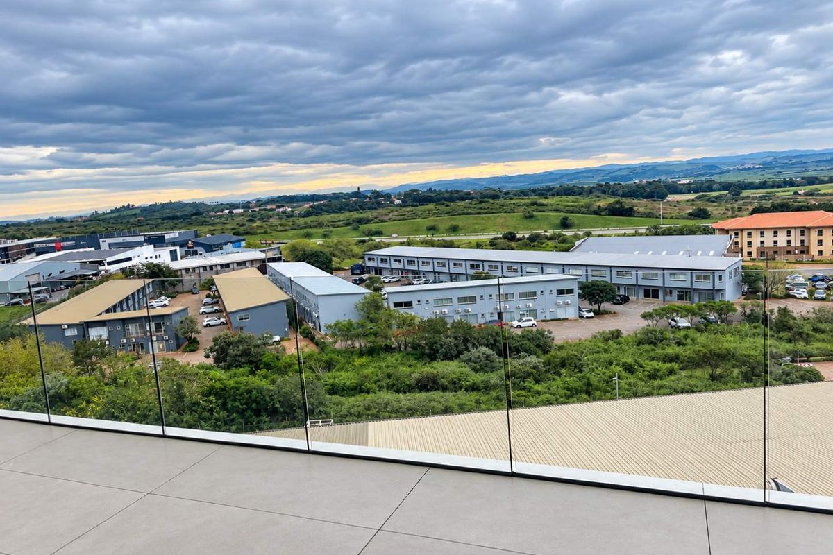 Elevated aerial view overlooking a commercial business park complex with surrounding green landscape and distant hills.