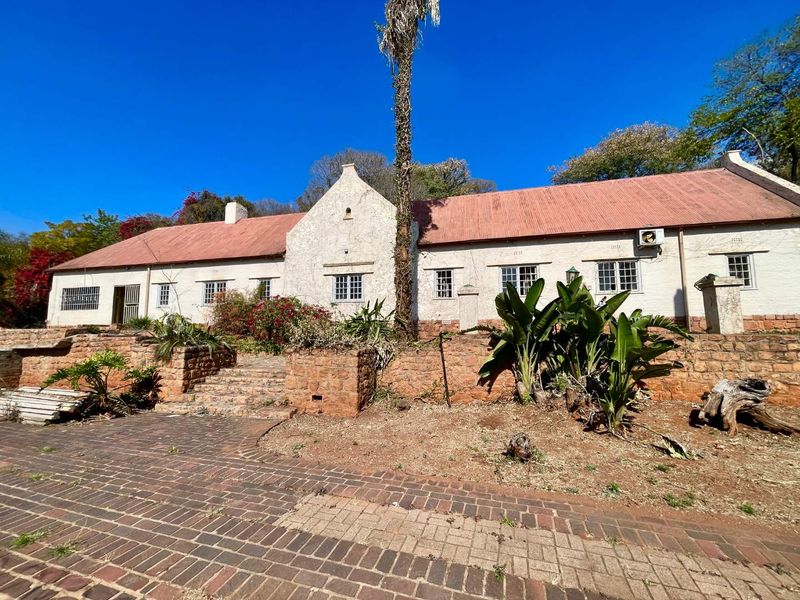 Rear view of a traditional house featuring a corrugated metal roof, stone retaining walls, and a brick-paved patio area.