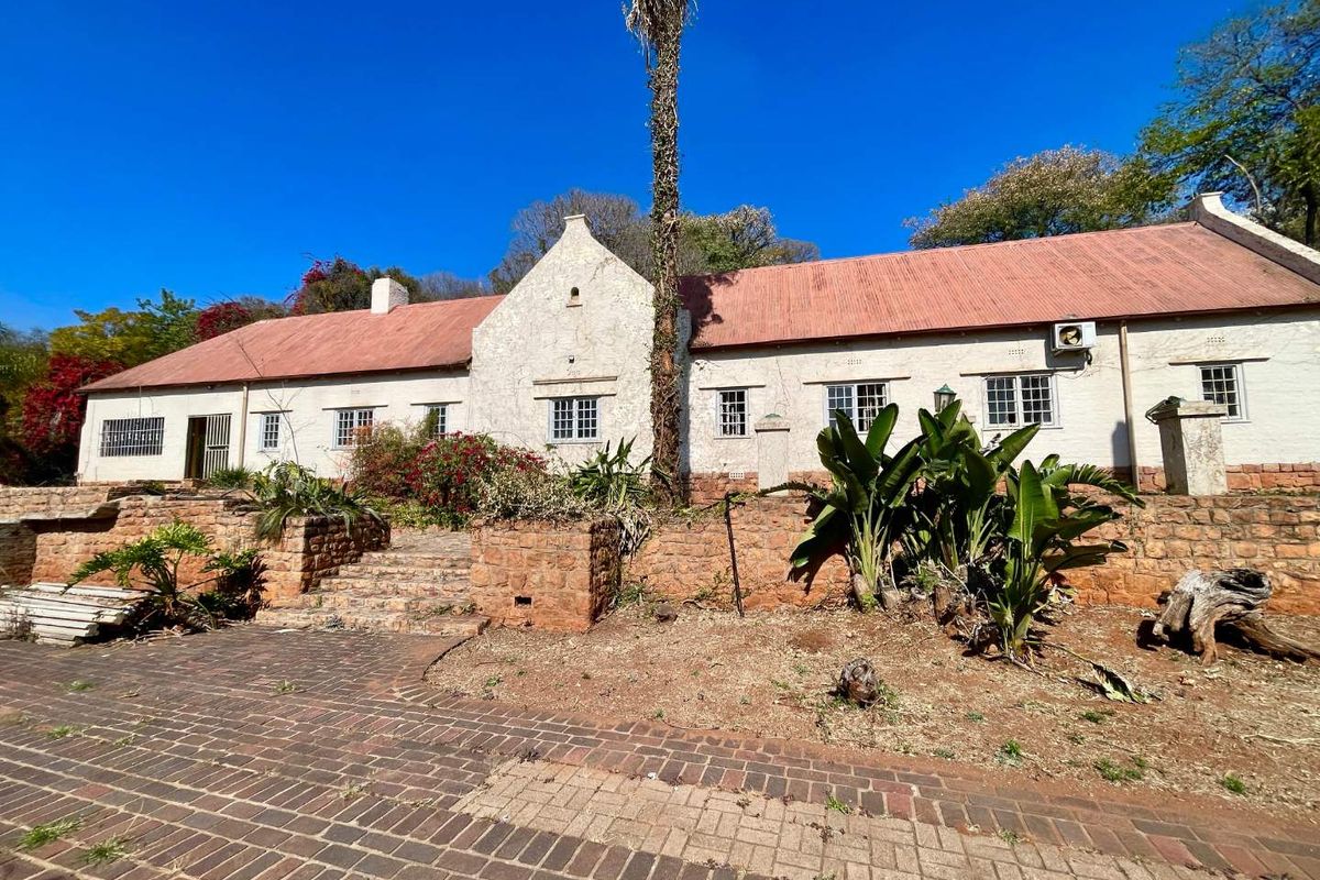Rear view of a traditional house featuring a corrugated metal roof, stone retaining walls, and a brick-paved patio area.
