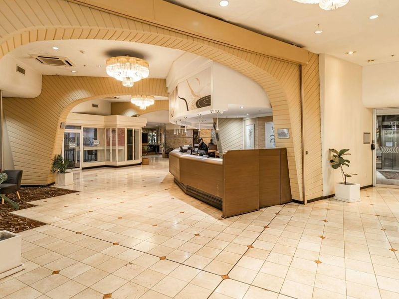 Spacious building entrance featuring a large reception desk, decorative architectural archways, tiled flooring, and bright recessed lighting.