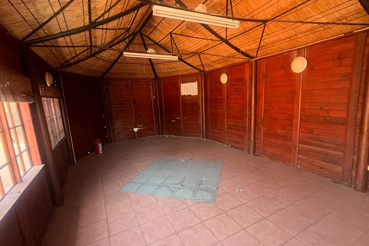 A rustic, timber-clad interior space featuring a vaulted thatched ceiling, tiled flooring, and large windows, suitable for a versatile living or recreational area.